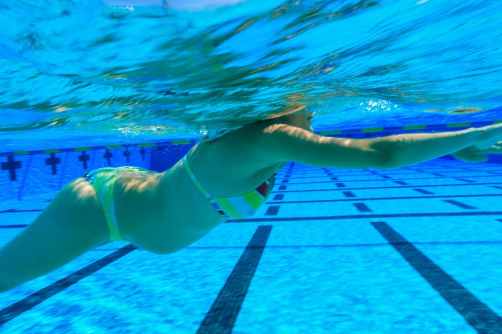 A woman in a bikini who is 24 weeks pregnant swimming in a pool with lanes.