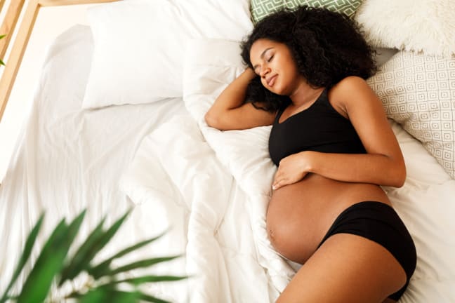 A 37 weeks pregnant woman wearing black underwear sleeping while holding her baby bump