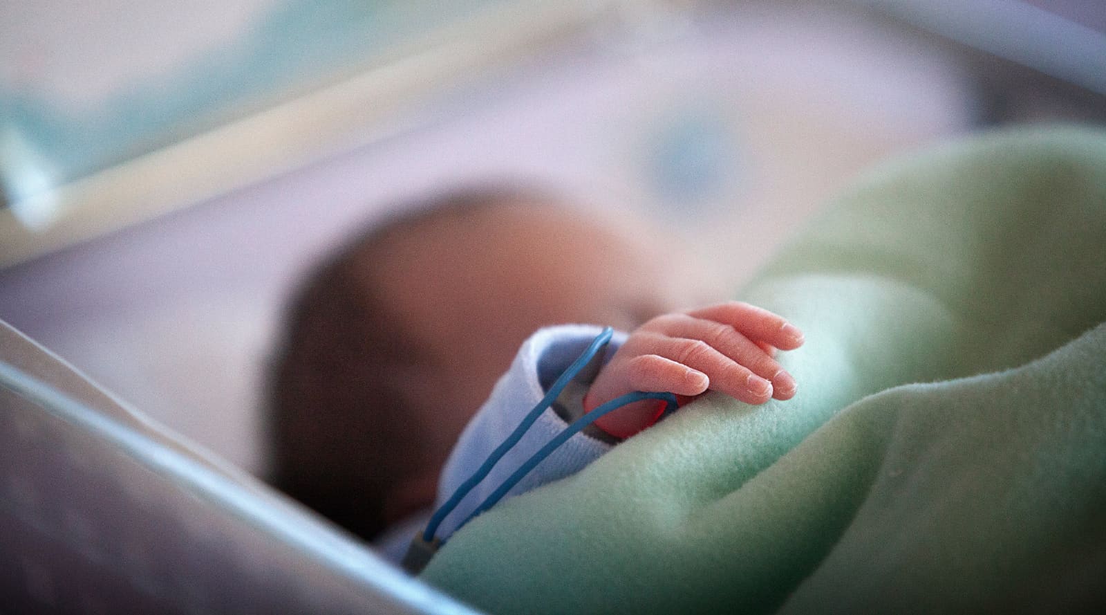 A preterm baby with a green blanket, resting in their bed