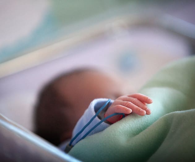A preterm baby with a green blanket, resting in their bed