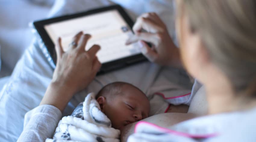 Mother breastfeeding a baby while using a tablet Mother breastfeeding a baby while using a tablet