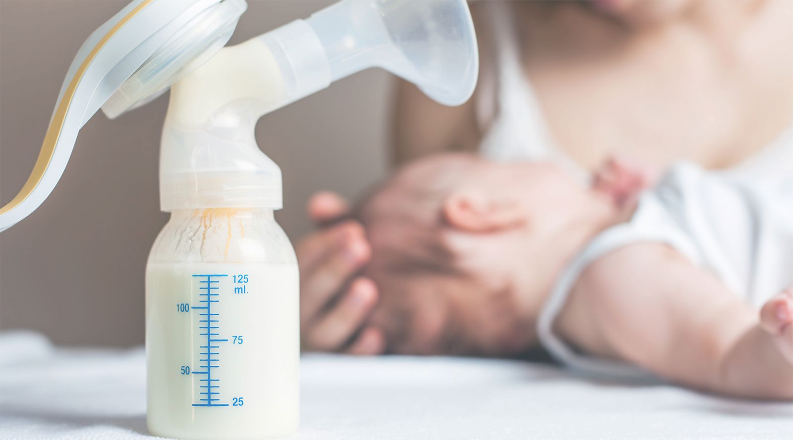 breast milk pump in the foreground and mother comforting her newborn baby in the background