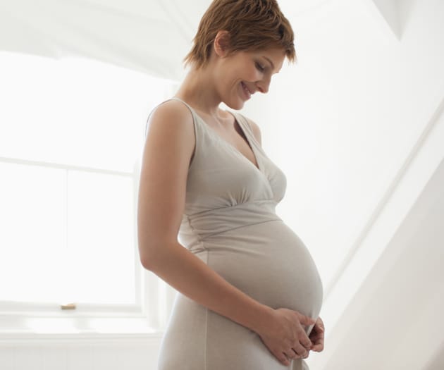 Pregnant mother smiling while looking down at her baby bump