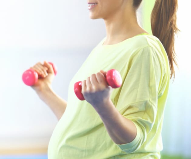 Pregnant mother sitting cross-legged in a prenatal barre lifting small dumbbells