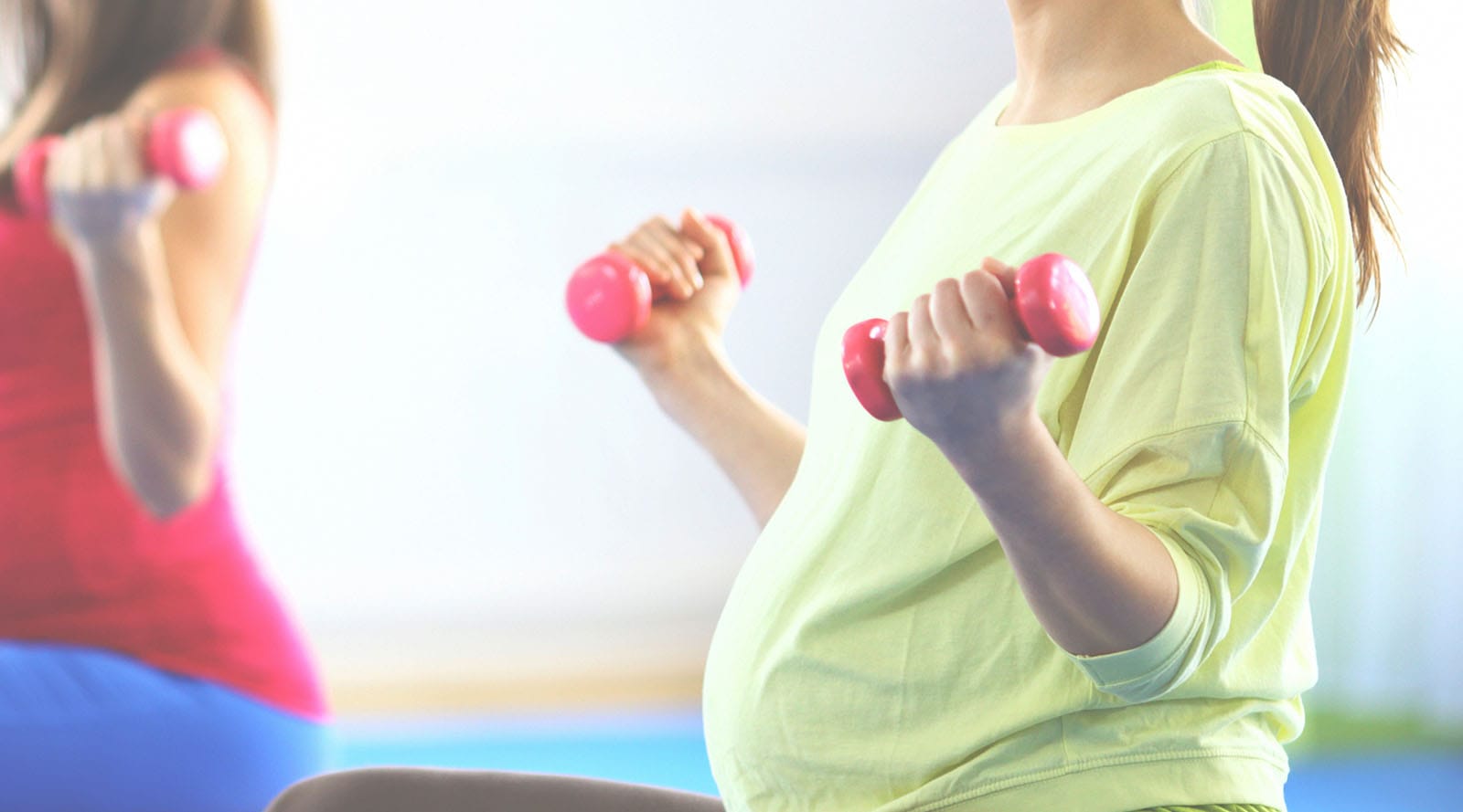 Pregnant mother sitting cross-legged in a prenatal barre lifting small dumbbells