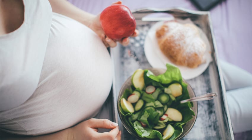 sma_pregnancydiet_body_1_850.jpg pregnant mother sitting with a food tray on her lap and an apple in her hand