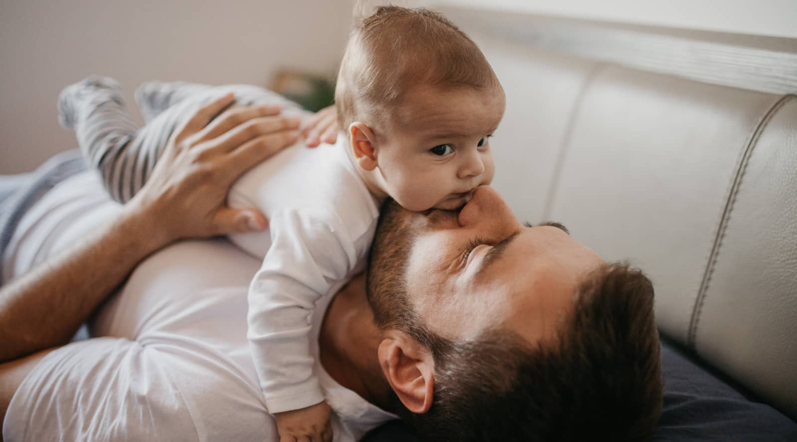 First time dad laying down and hugs newborn across his chest and giving kisses