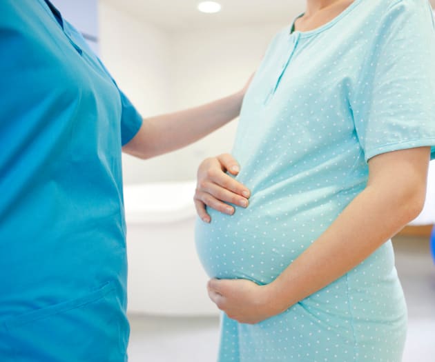 pregnant-mother-holding-baby-bump-speaking-to-nurse